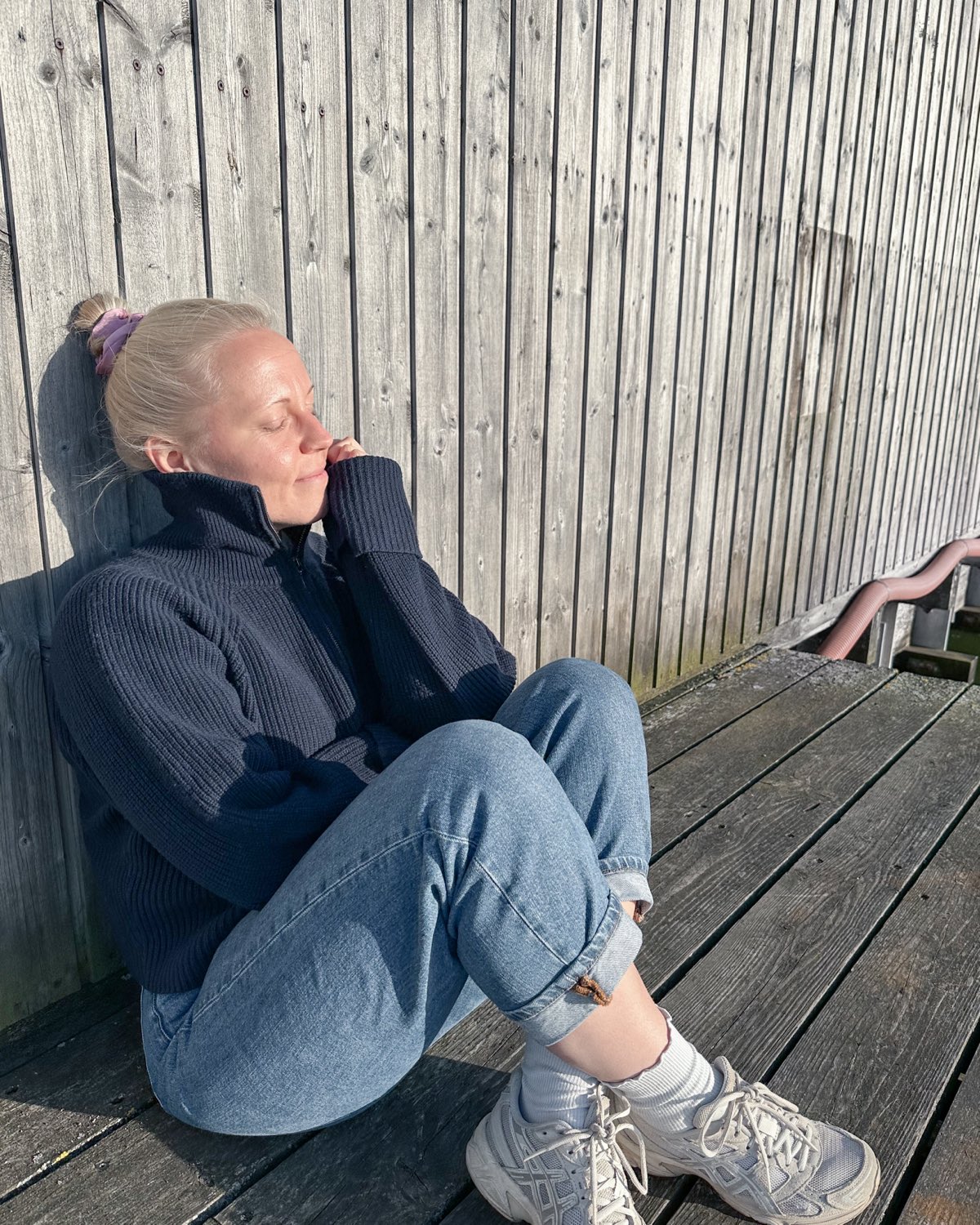 Marie sitzt in der Sonne an einer Holzwand in Dänemark